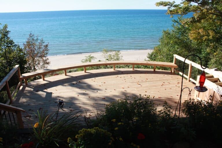 Forget standard backyard deck shapes. Precision creates custom decks that meet the needs of our customers. The view from the second tier of an elevated deck built along the back of a house near the shores of Lake Michigan. The deck is curved to fill the space between the trees.